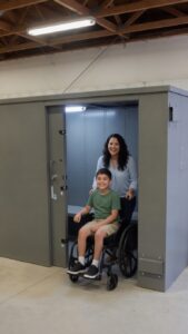 Mother and child in a wheelchair standing beside an accessible above-ground tornado shelter installed by Absolute Building Concepts in the Kansas City area.