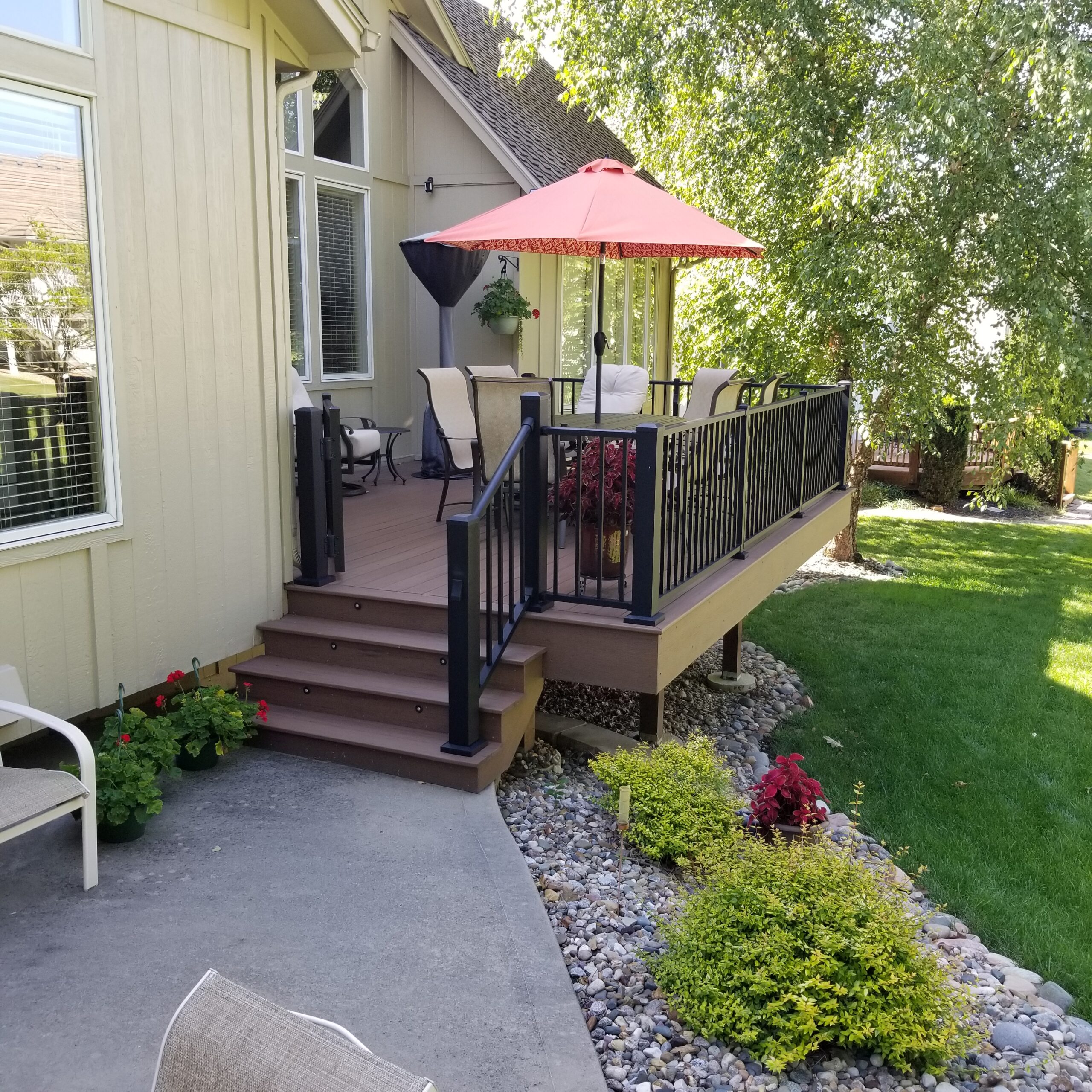 Composite backyard deck with composite railing, outdoor furniture, and patio umbrella, creating a comfortable outdoor living space.